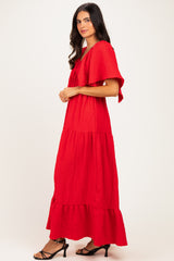 woman wearing a red tiered maxi dress with ruffle sleeves and a bow detail, standing sideways against a plain background