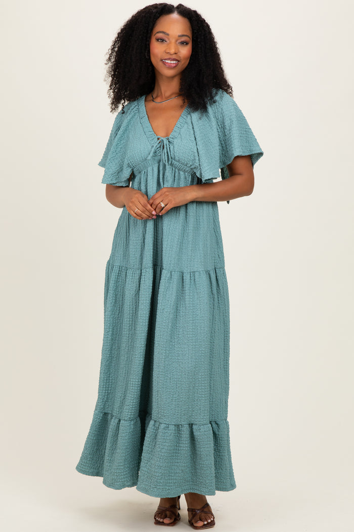 woman wearing a teal tiered maxi dress with flutter sleeves and a drawstring neckline