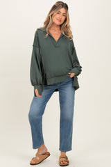 woman wearing a dark green maternity top with a v-neck and long sleeves paired with light blue jeans
