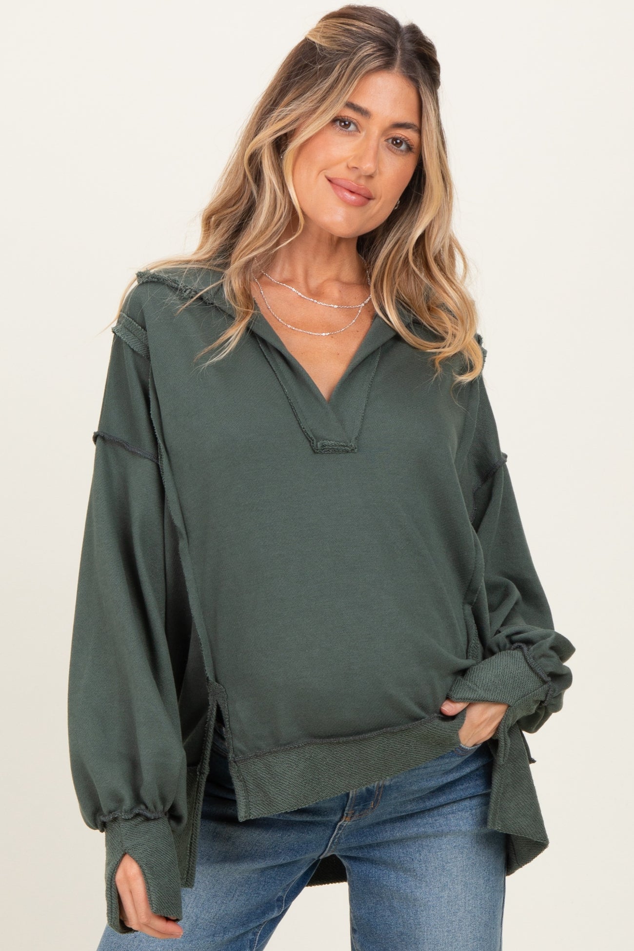 woman wearing a dark green maternity pullover with a v-neck and loose sleeves, styled with casual blue jeans