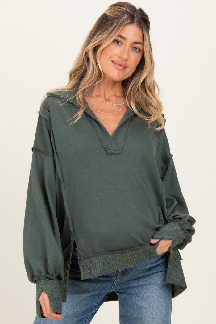 woman wearing a dark green maternity pullover with a v-neck and loose sleeves, styled with casual blue jeans
