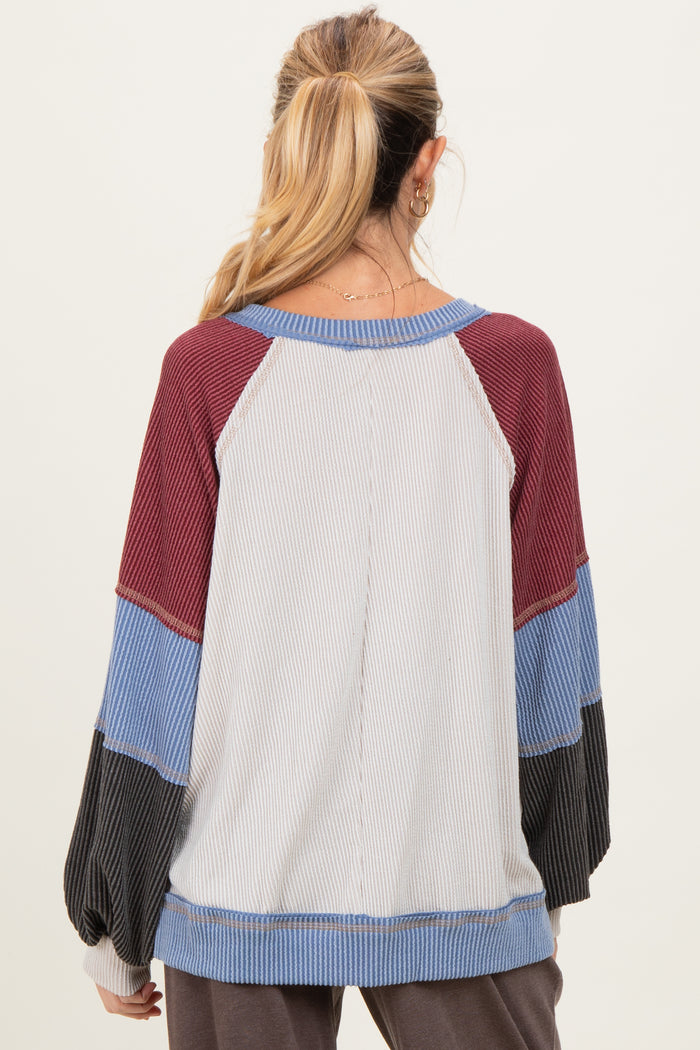 woman wearing a maternity color block long sleeve top in gray, maroon, blue, and black with a relaxed fit and balloon sleeves