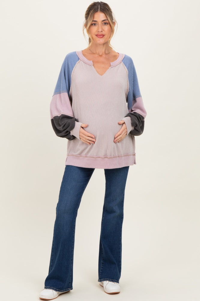 woman wearing a multicolored ribbed maternity top with a v-neck and holding her baby bump, paired with flared jeans