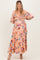 woman wearing a floral patterned pink maternity dress with long sleeves and tiered skirt, showcasing a baby bump