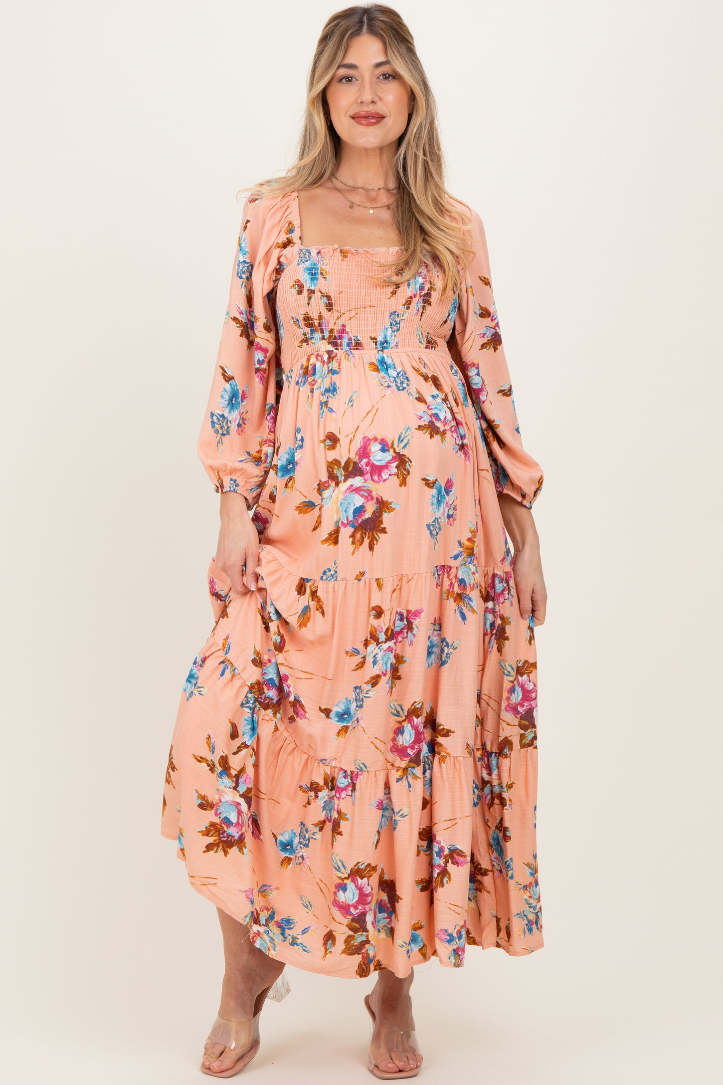woman wearing a blush floral maternity maxi dress with puff sleeves and a smocked bodice, displaying her baby bump