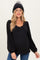 woman wearing a black ribbed maternity top with a scoop neckline and long puff sleeves, styled with a black knit beanie