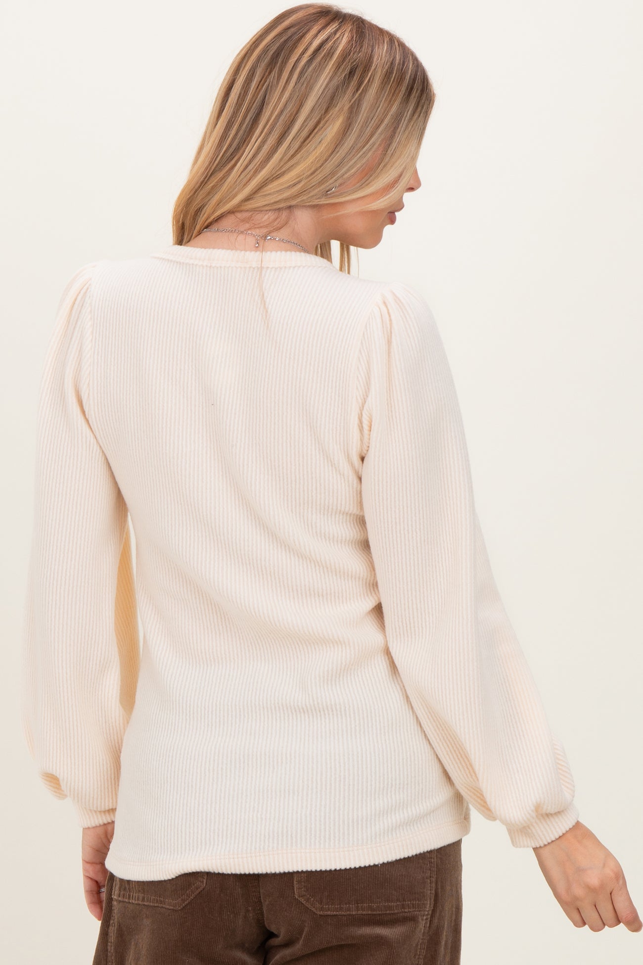 woman wearing a pale peach ribbed long sleeve top with puffed sleeves, viewed from the back
