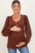 woman wearing a rust ribbed maternity top with puffy sleeves, holding her baby bump