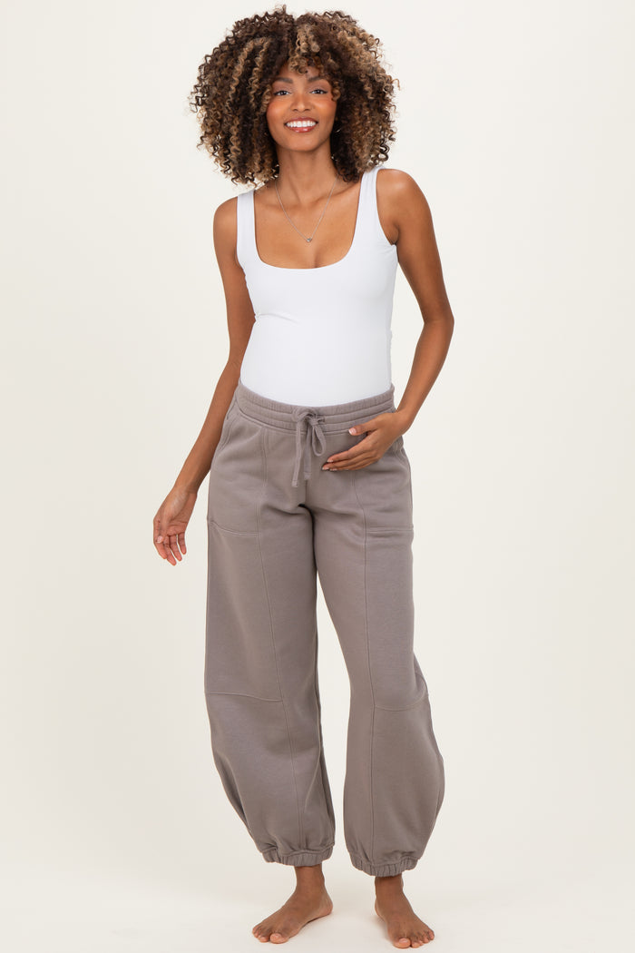woman wearing a white scoop neck bodysuit and gray maternity joggers, showing off her baby bump