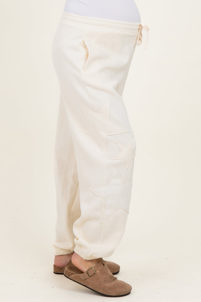 woman wearing cream maternity joggers with star embroidery and a drawstring waist, showcasing her baby bump
