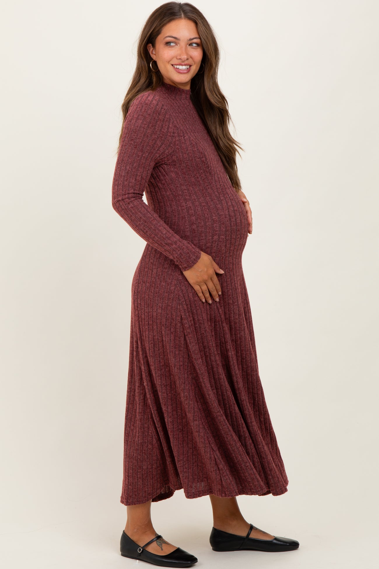 woman wearing a rust ribbed long sleeve maternity dress, gently holding her baby bump