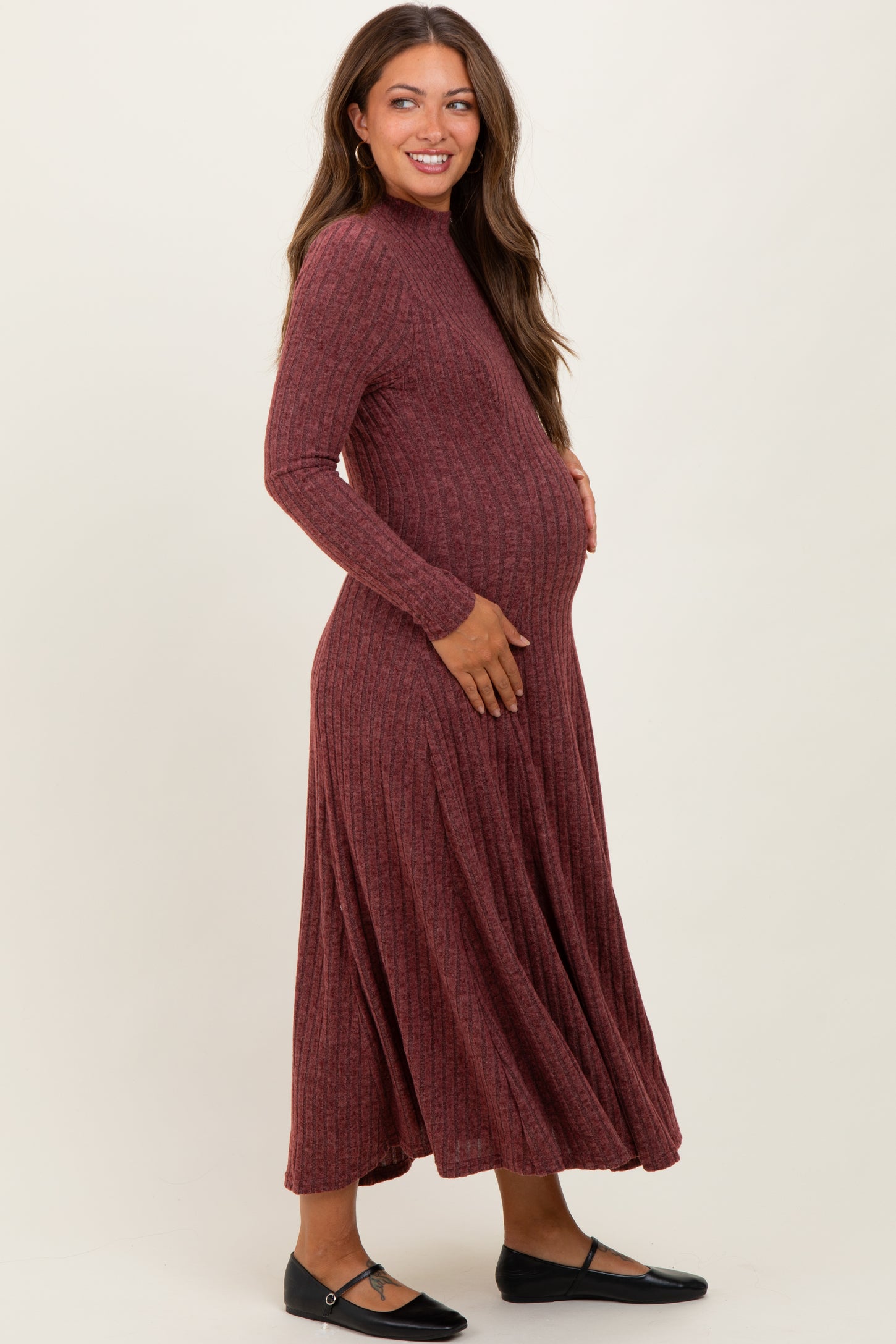 woman wearing a rust ribbed long sleeve maternity dress, gently holding her baby bump