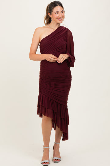 woman wearing a burgundy one-shoulder maternity dress with ruched details and a ruffled hem