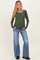 woman wearing a dark green long sleeve maternity top and distressed blue jeans, showcasing her baby bump