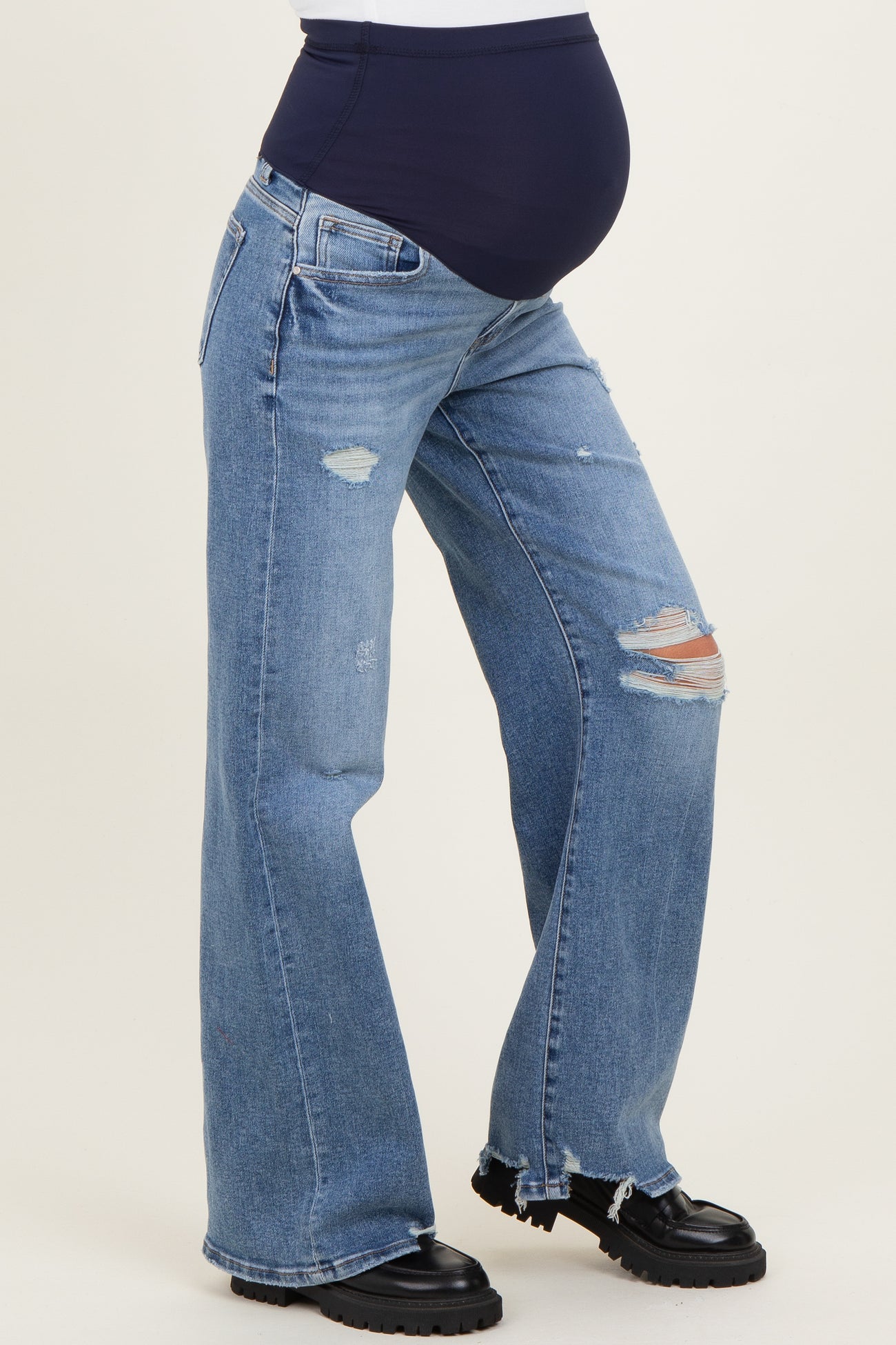 woman wearing distressed blue maternity jeans with a navy belly panel and a visible baby bump