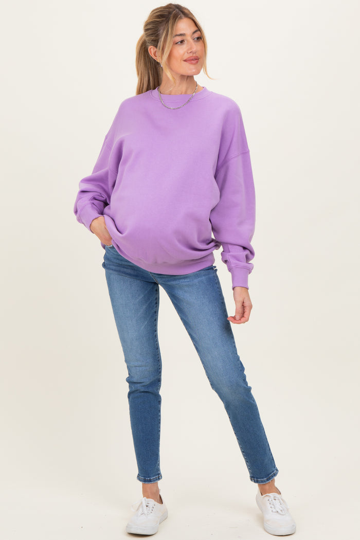 woman wearing a purple oversized sweatshirt and blue skinny jeans, showcasing a visible baby bump