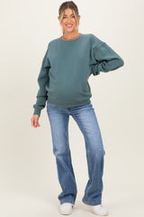 woman wearing a teal oversized maternity sweatshirt with long sleeves and distressed light blue jeans, showing her baby bump
