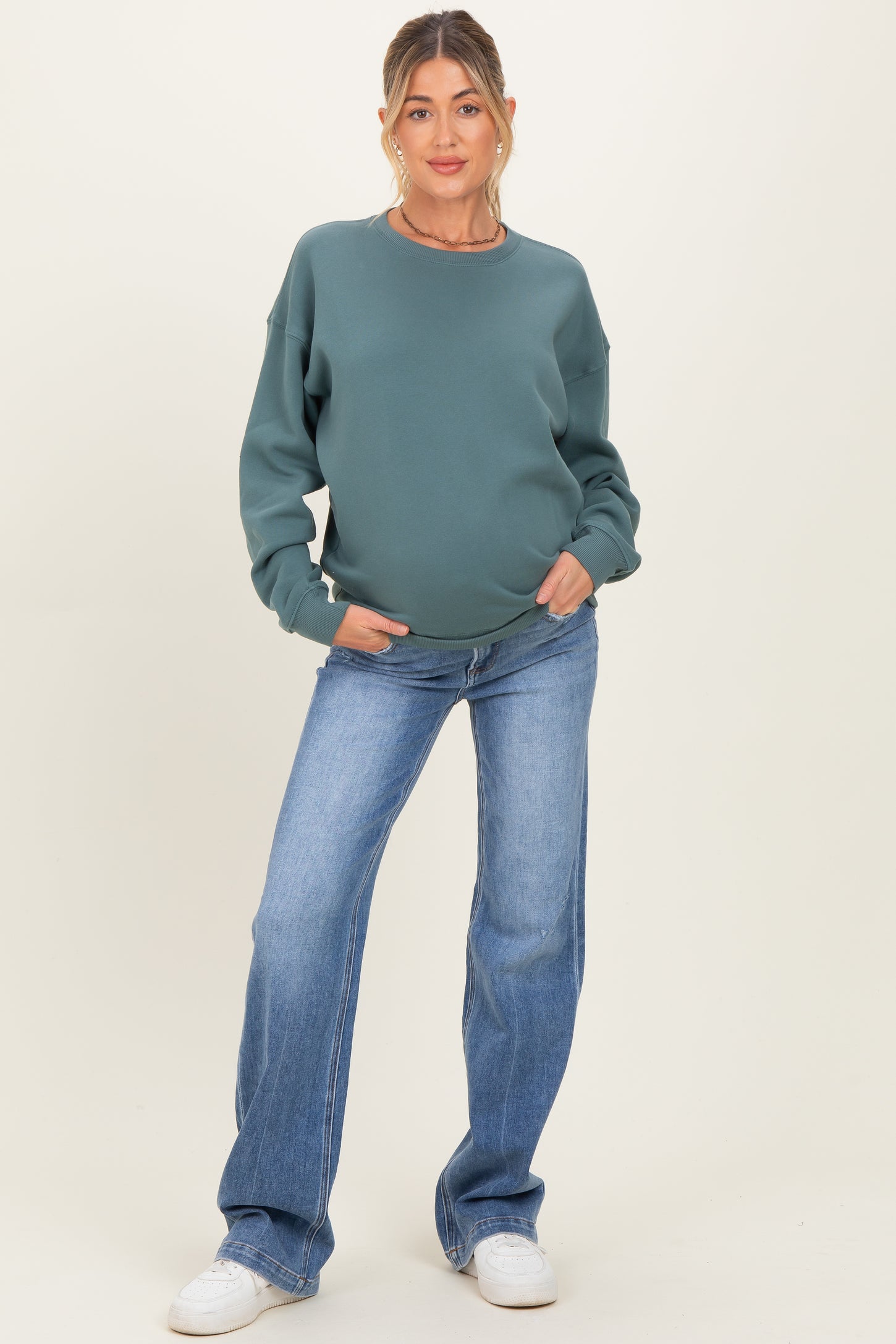 woman wearing a green maternity sweatshirt and blue flared jeans, baby bump visible