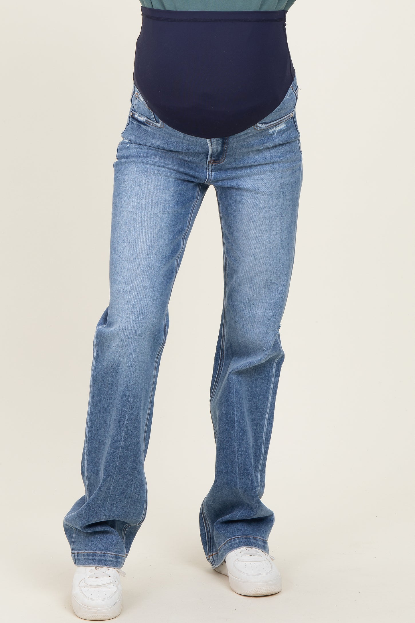 woman wearing blue maternity jeans with a dark blue belly panel and a relaxed fit, paired with white sneakers