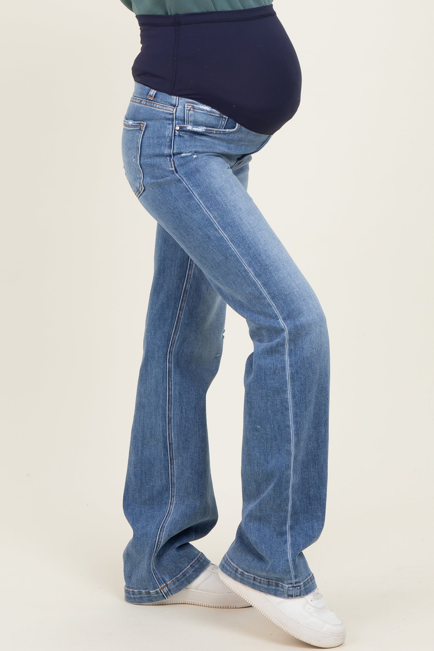 woman wearing blue flared maternity jeans with a fitted belly panel and showing off her baby bump