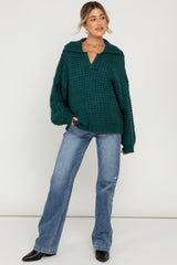 woman wearing a dark green cozy knit maternity sweater with a collar, paired with light blue flared jeans