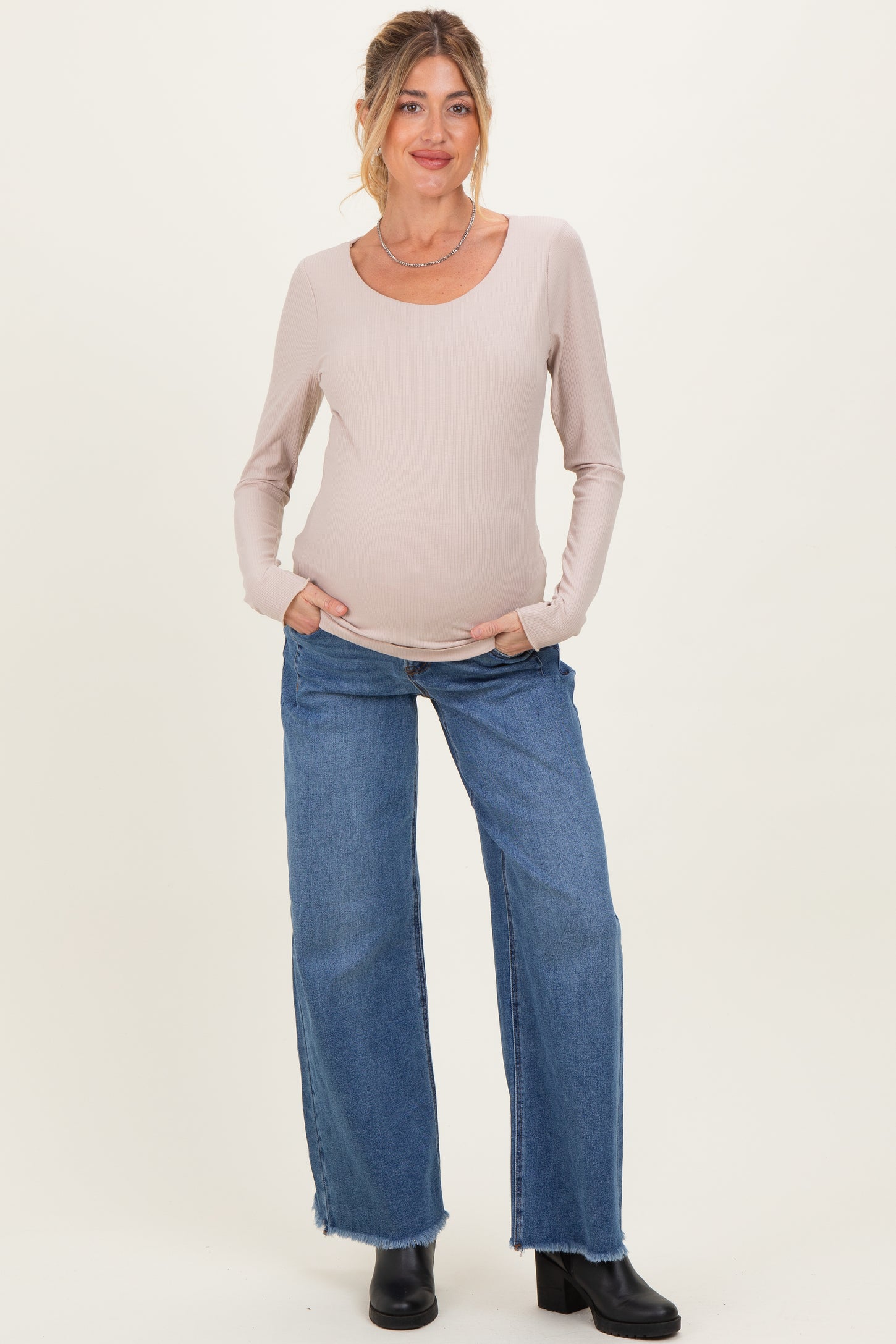 woman wearing a beige ribbed long sleeve maternity top with a baby bump and blue wide-leg jeans