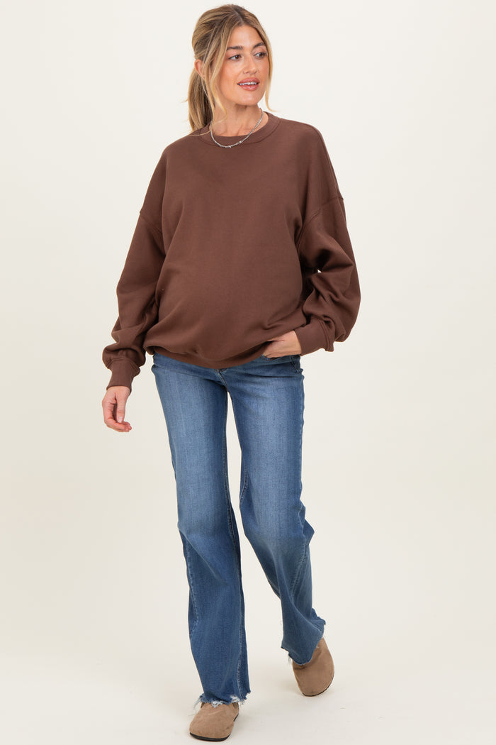 woman wearing a brown maternity sweatshirt and blue flared jeans with a visible baby bump