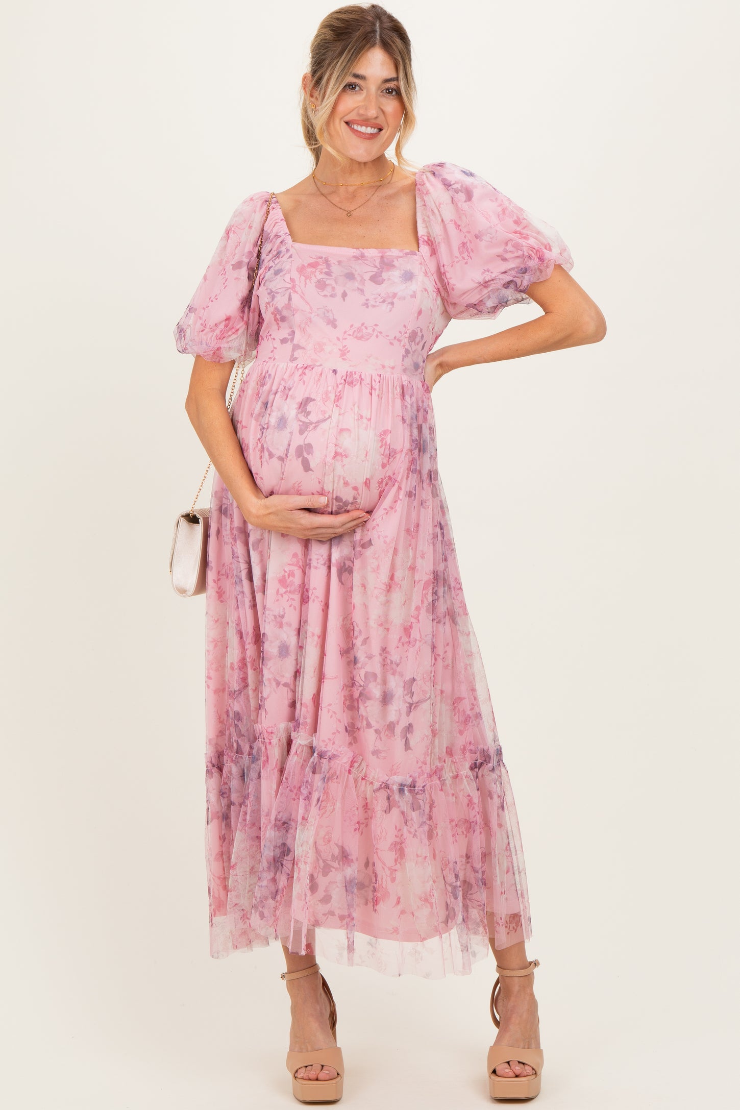 woman wearing a pink floral maternity dress with puff sleeves and a flowing skirt, posing with her baby bump