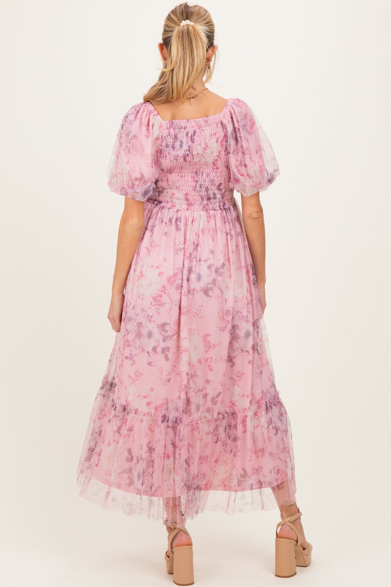 woman wearing a floral pink maternity dress with puff sleeves and a flowy skirt, standing with her back to the camera