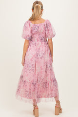 woman wearing a floral pink maternity dress with puff sleeves and a flowy skirt, standing with her back to the camera
