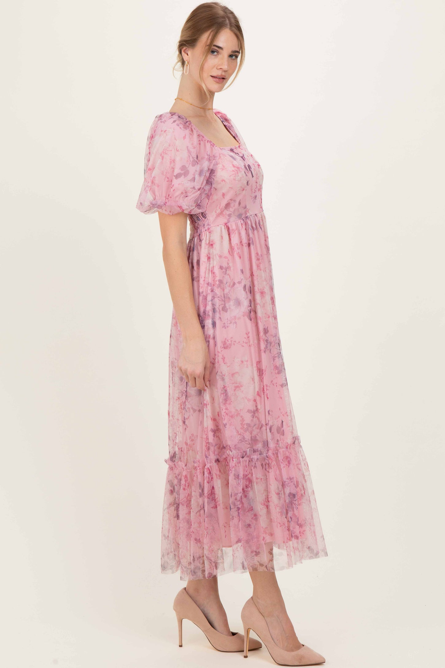 woman wearing a pink floral midi dress with puff sleeves and a tiered ruffled hem, standing in profile