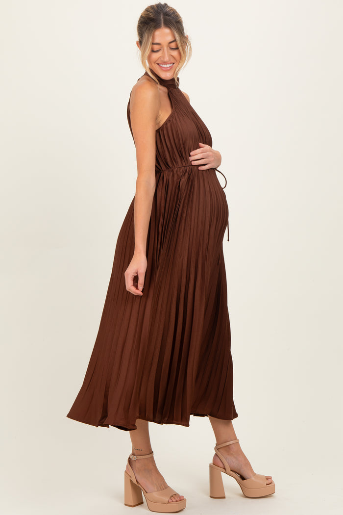 woman wearing a brown pleated maternity dress featuring a tie waist and showing her baby bump