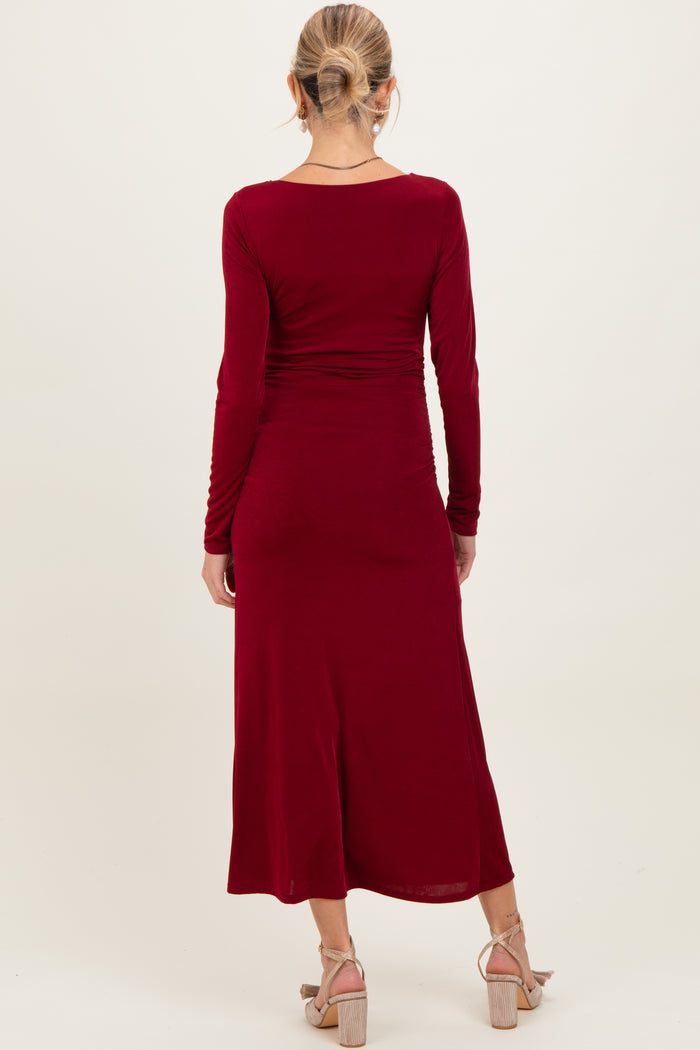 woman wearing a burgundy long sleeve maternity dress with a fitted silhouette and ruching on the sides