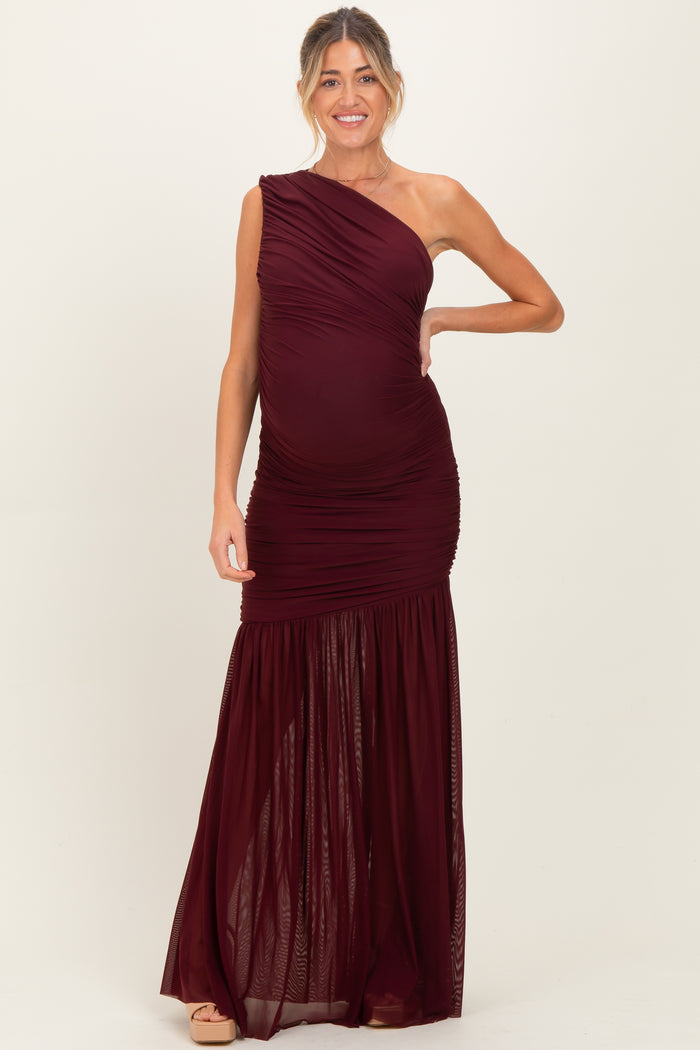 woman wearing a burgundy one-shoulder maternity gown with ruching and a flowy skirt, showcasing her baby bump