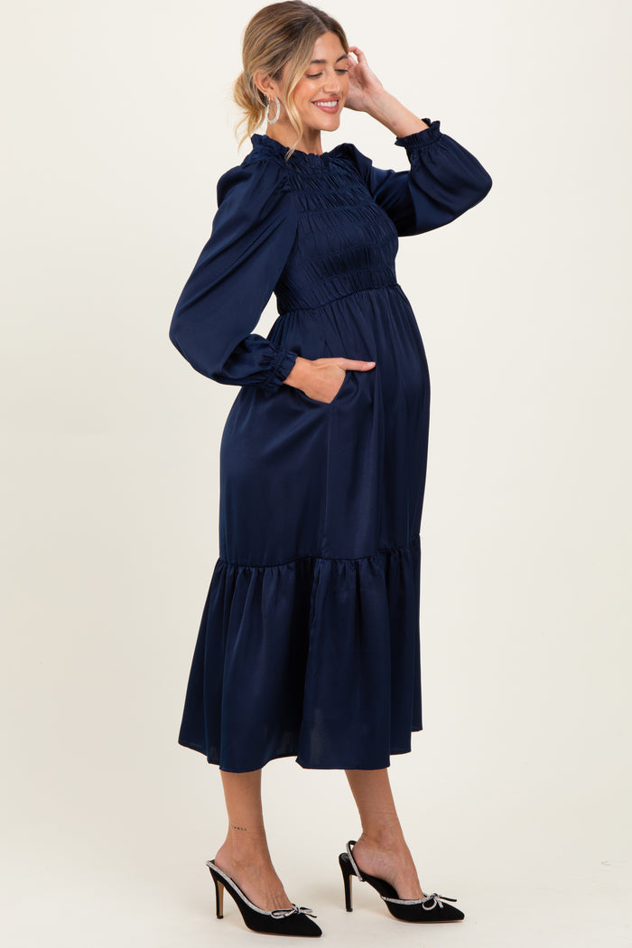 woman wearing a navy blue maternity dress with smocked bodice, long sleeves, and tiered skirt, showing her baby bump