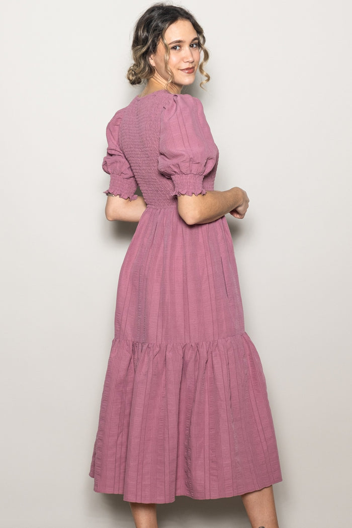 woman wearing a dusty pink midi dress with puff sleeves and a tiered skirt, shown from the back