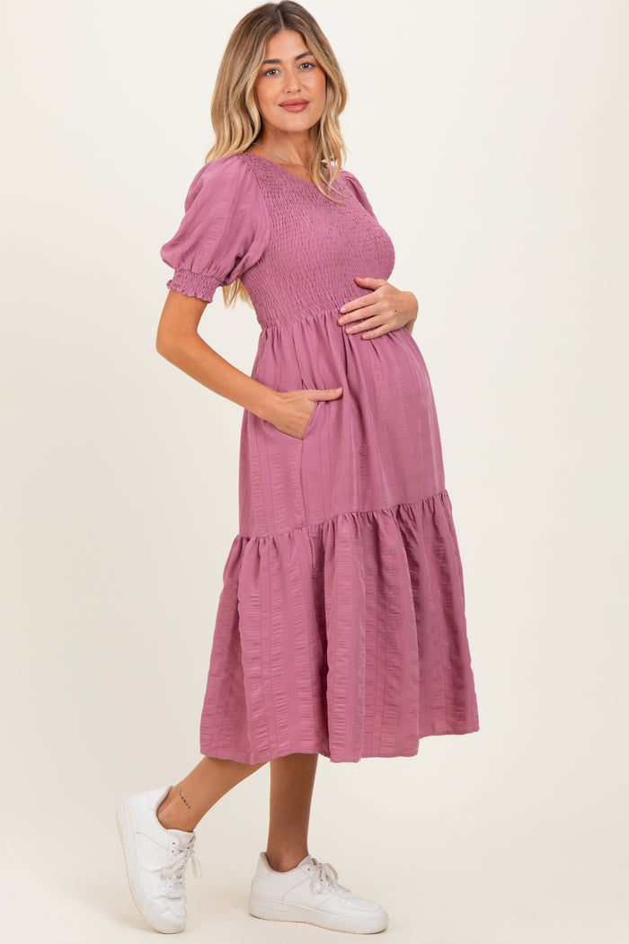woman wearing a pink smocked maternity dress with puff sleeves and pockets, gently cradling her baby bump