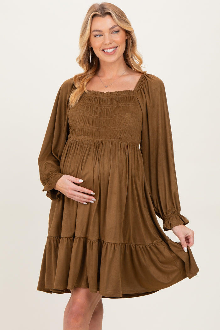 woman wearing a brown maternity dress with smocked bodice and tiered skirt, gently cradling her baby bump
