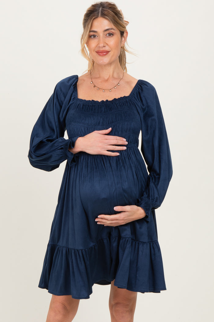 woman wearing a navy blue maternity dress with puff sleeves and a ruffled hem, holding her baby bump