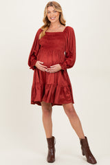 woman wearing a rust-colored maternity dress with puff sleeves and a tiered hem, gently holding her baby bump