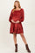 woman wearing a rust-colored maternity dress with puff sleeves and a tiered hem, gently holding her baby bump