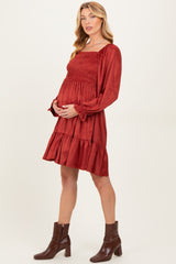woman wearing a rust colored maternity dress with long sleeves, smocked bodice, and tiered skirt, holding her baby bump
