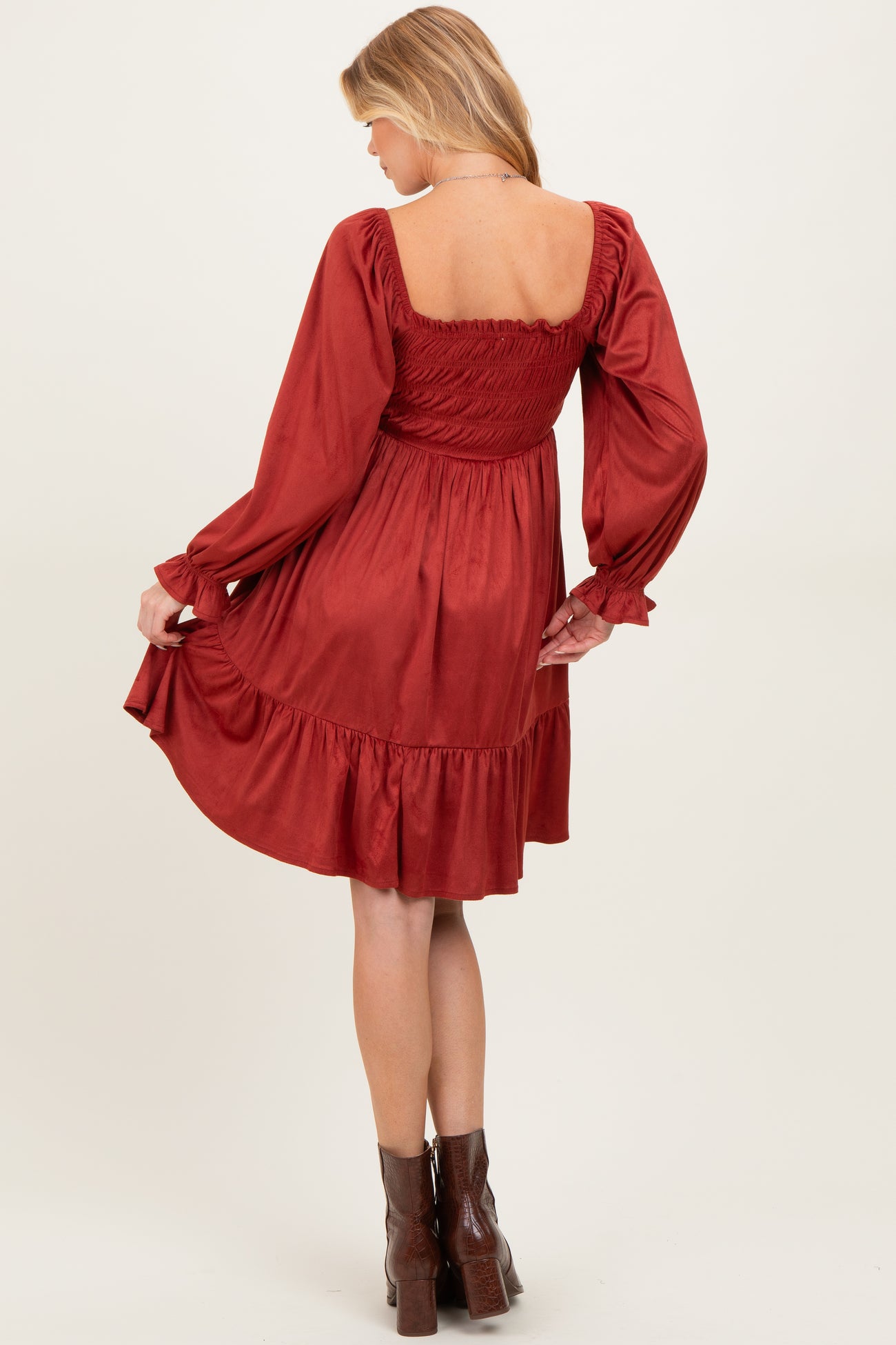 woman wearing a rust-colored maternity dress with a smocked bodice and long sleeves, showing a flared skirt