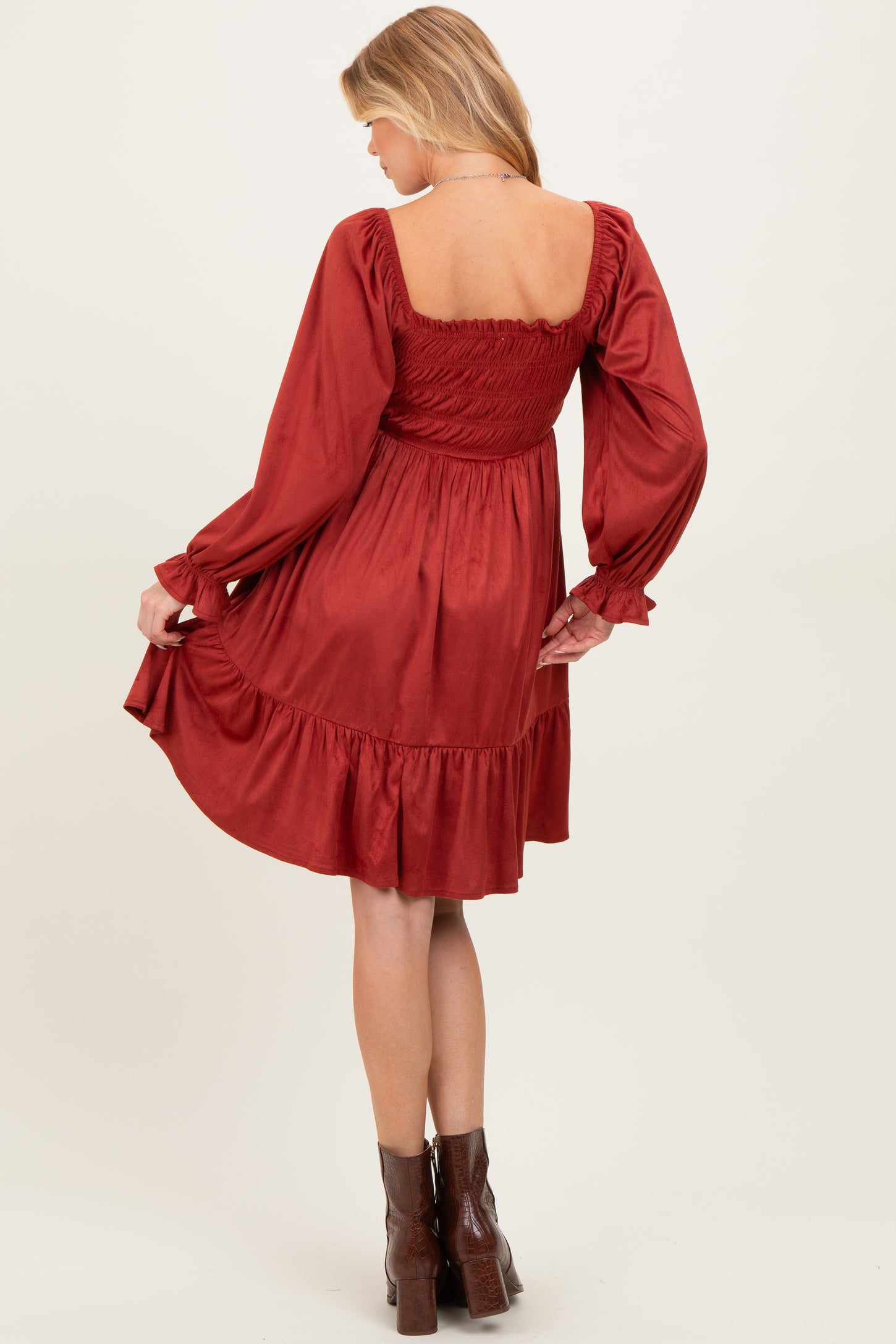 woman wearing a rust-colored maternity dress with a smocked bodice and long sleeves, showing a flared skirt