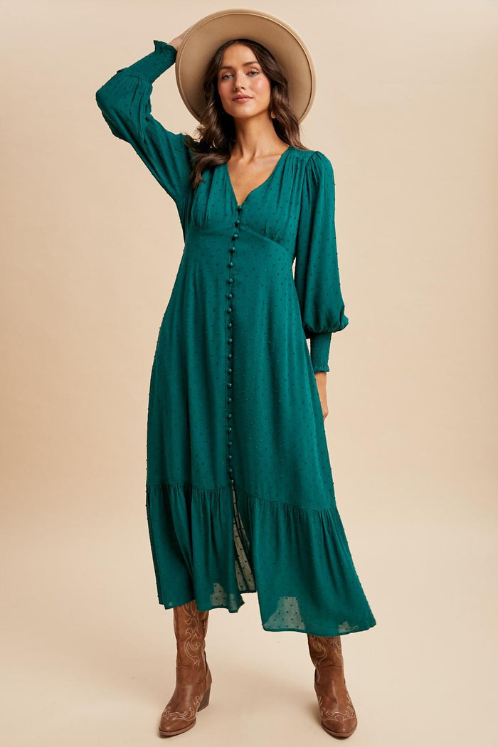 woman wearing a green long sleeve button-down dress with a tiered skirt and a wide-brimmed hat, paired with brown boots