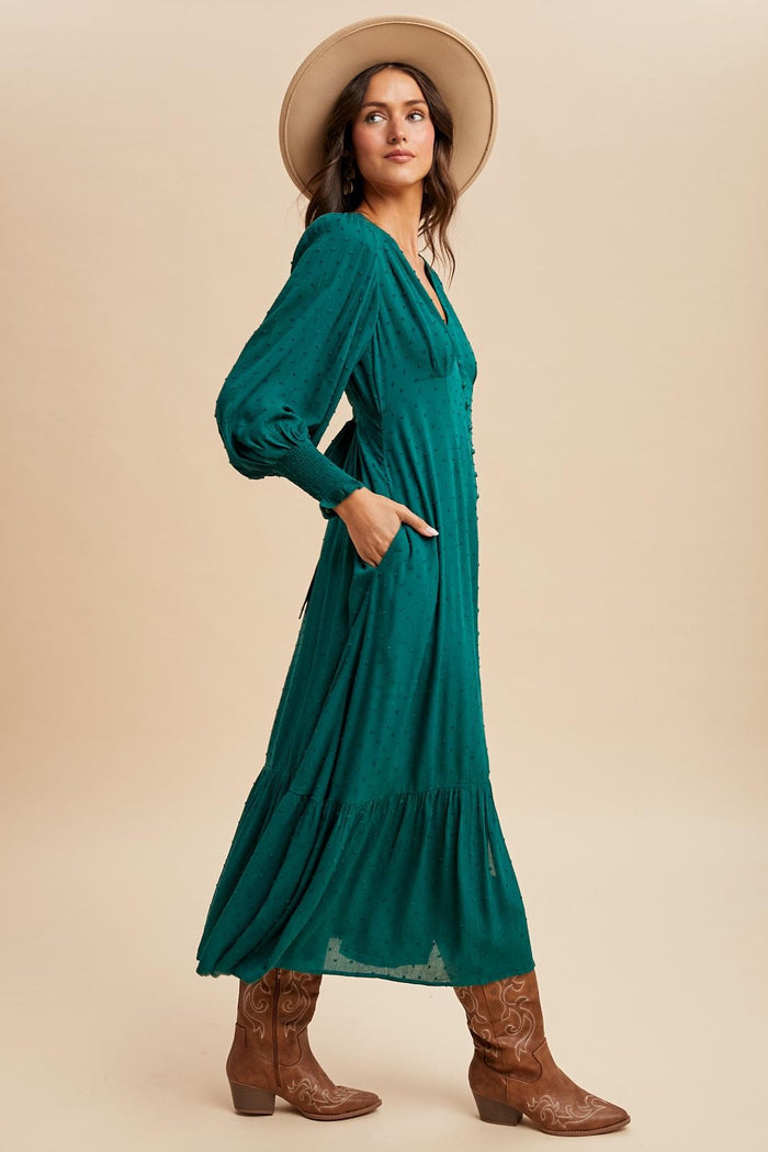woman wearing a teal long sleeve maxi dress with a tiered skirt and pockets, paired with brown cowboy boots and a wide-brim hat