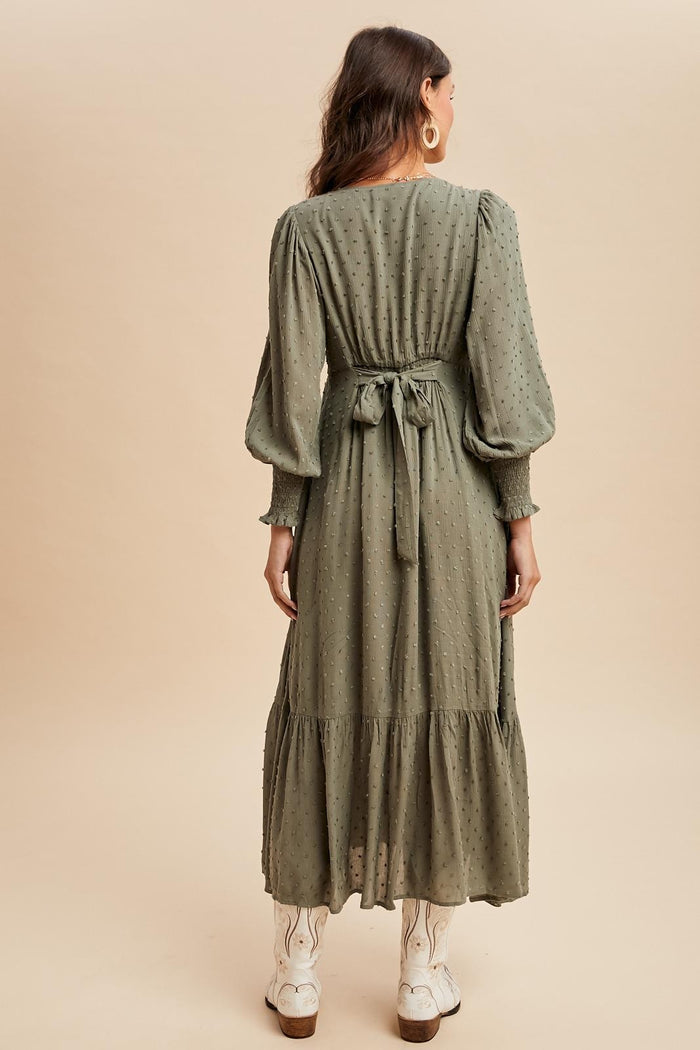 woman wearing a long olive green tiered maxi dress with puff sleeves and a tied waist detail, seen from the back