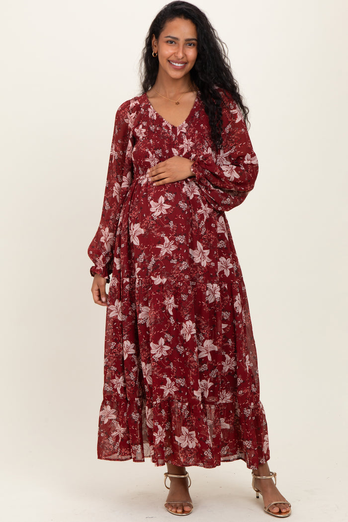 woman wearing a burgundy floral maxi maternity dress and holding her baby bump