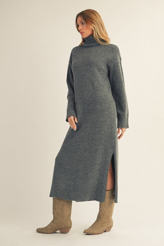 woman wearing a long gray sweater dress with a high neck and side slit, paired with tan knee-high boots