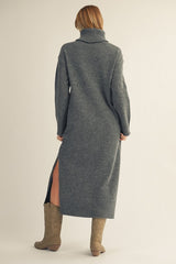woman wearing a long gray sweater dress with a high neck and side slits, complemented by tall beige boots